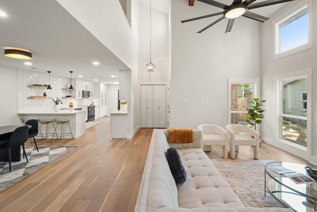 living room featuring light wood-style floors, baseboards, a high ceiling, recessed lighting, and a ceiling fan