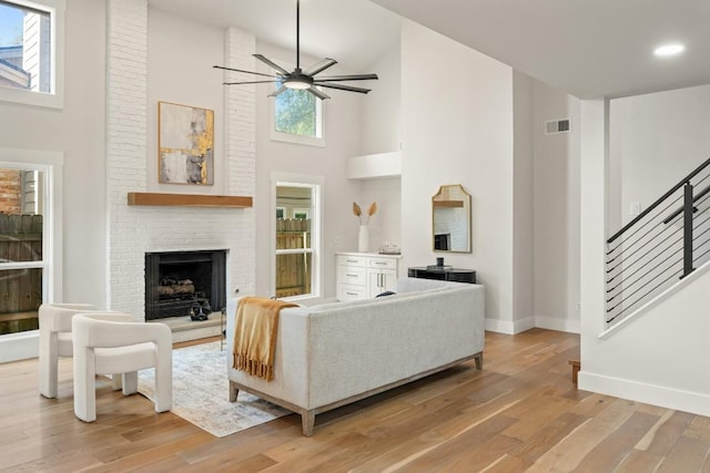 living room featuring light wood-style floors, high vaulted ceiling, ceiling fan, and a fireplace