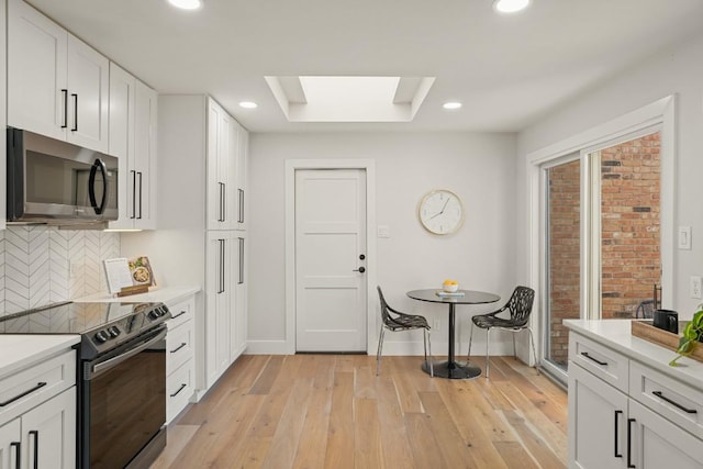 kitchen with backsplash, light wood-type flooring, light countertops, stainless steel microwave, and black range with electric cooktop