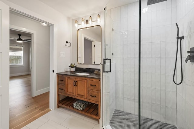 bathroom featuring vanity, wood finished floors, baseboards, tiled shower, and a ceiling fan