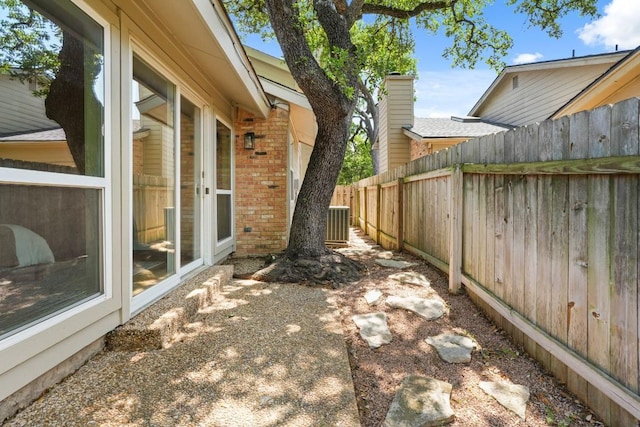 exterior space featuring brick siding, fence, and central AC unit