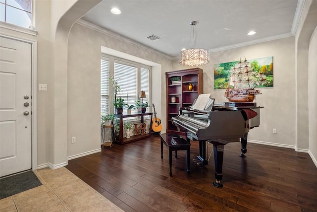 foyer entrance with crown molding, a chandelier, baseboards, visible vents, and hardwood / wood-style flooring