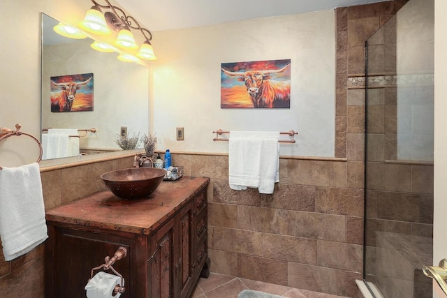 full bathroom featuring vanity, tile patterned flooring, tile walls, tiled shower, and a wainscoted wall
