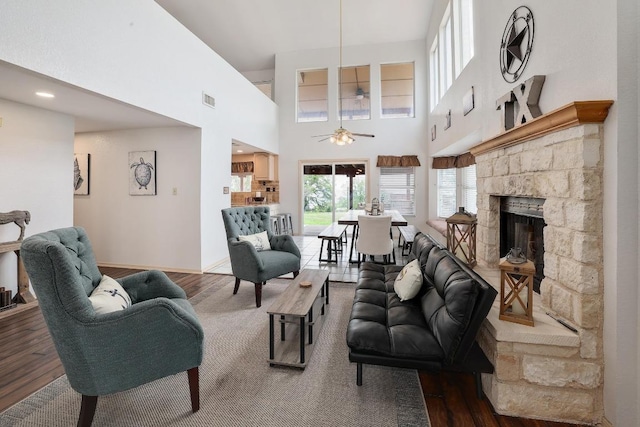 living area featuring a stone fireplace, a ceiling fan, wood finished floors, and visible vents