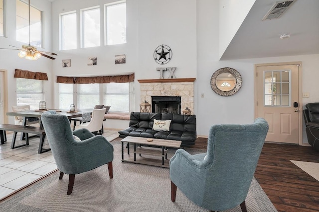 living room with visible vents, a towering ceiling, wood finished floors, a fireplace, and a ceiling fan