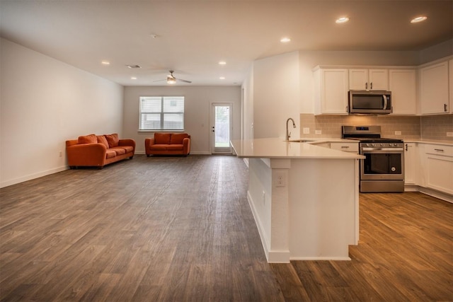 kitchen featuring a peninsula, open floor plan, white cabinetry, a sink, and appliances with stainless steel finishes