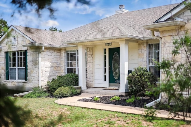 view of exterior entry with a shingled roof, a chimney, and stone siding