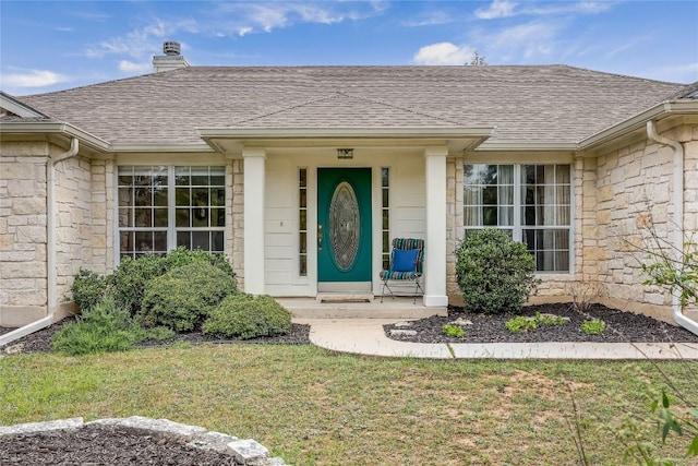 entrance to property featuring roof with shingles, a chimney, a lawn, and stone siding