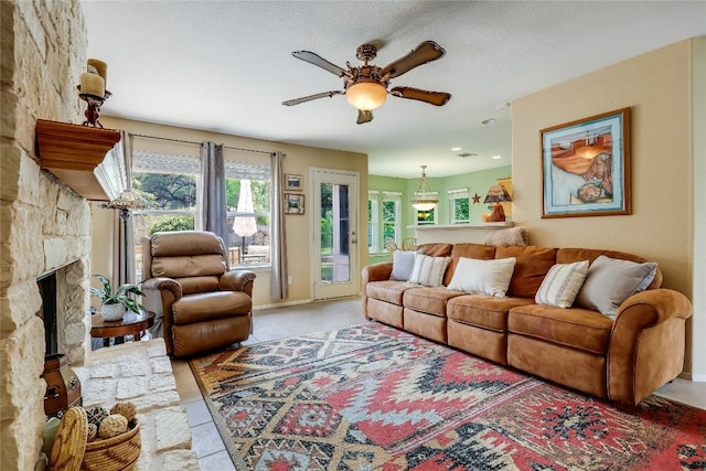 tiled living area featuring a ceiling fan, baseboards, and a stone fireplace