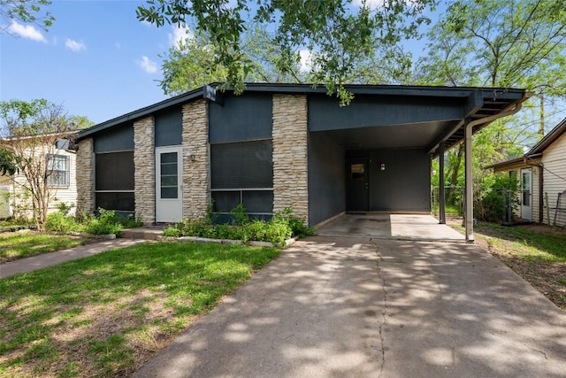 view of front facade featuring an attached carport, concrete driveway, a front yard, and stone siding
