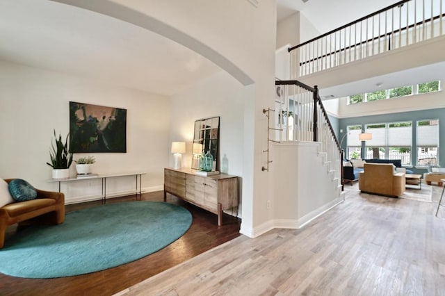 foyer entrance with stairs, arched walkways, baseboards, and wood finished floors