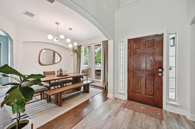 entrance foyer featuring visible vents, wood finished floors, baseboards, a chandelier, and arched walkways