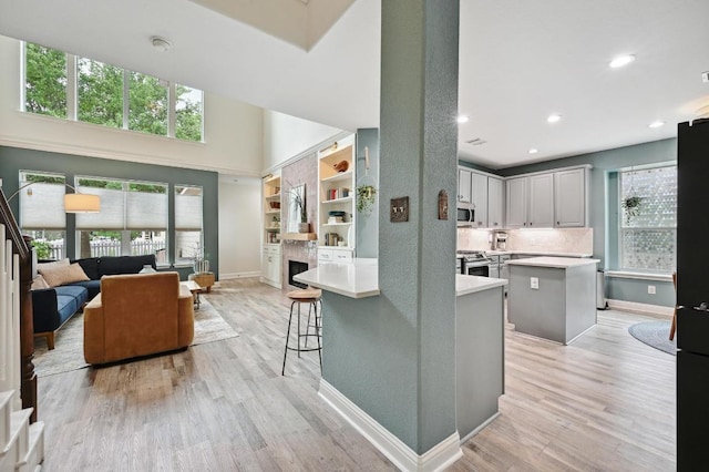 kitchen with stainless steel stove, light countertops, baseboards, open floor plan, and light wood-type flooring