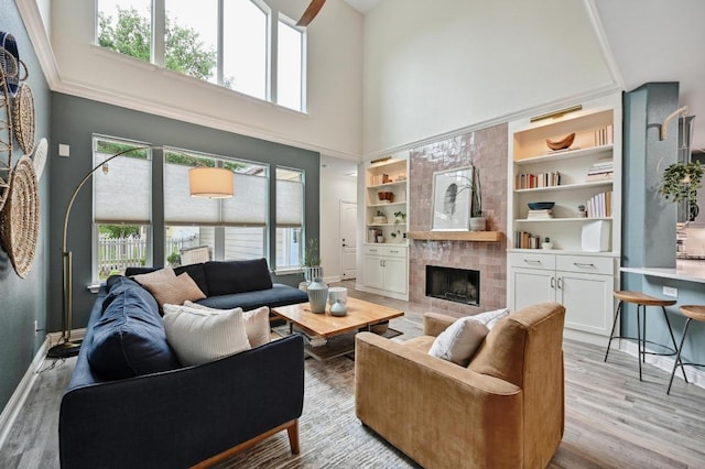 living area featuring baseboards, light wood-style flooring, a high ceiling, and a tile fireplace