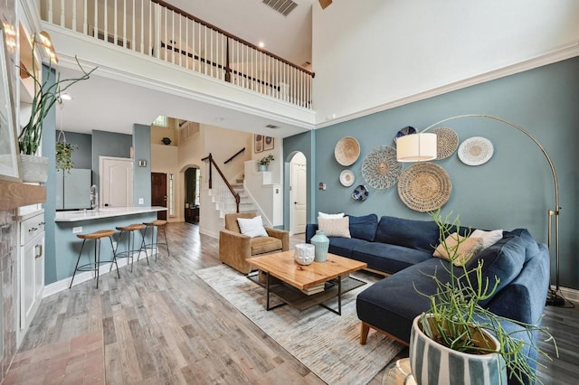 living area featuring visible vents, stairs, a towering ceiling, wood finished floors, and arched walkways