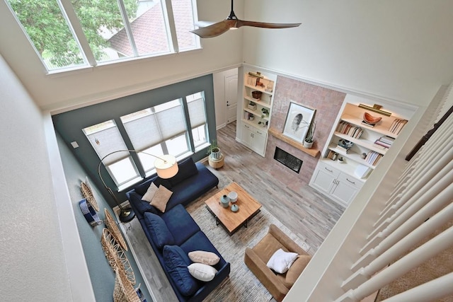 living room featuring light wood-type flooring, a healthy amount of sunlight, a tiled fireplace, and a towering ceiling
