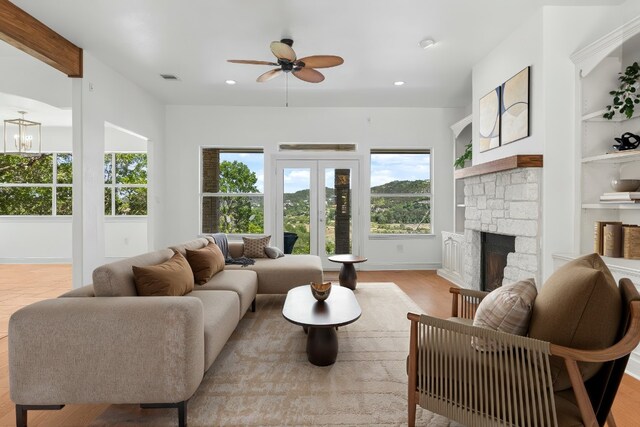 living room with a stone fireplace, ceiling fan with notable chandelier, recessed lighting, wood finished floors, and visible vents
