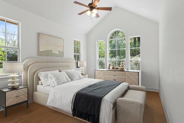 bedroom featuring a ceiling fan, high vaulted ceiling, multiple windows, and wood finished floors