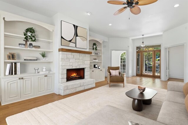 living room featuring built in features, ceiling fan, a fireplace, and light wood-type flooring