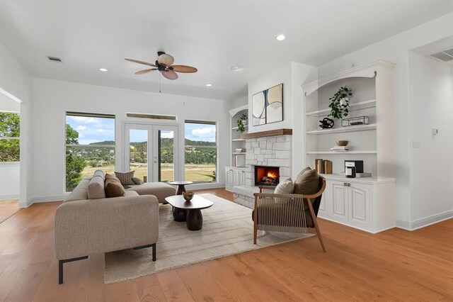 living area with ceiling fan, a stone fireplace, visible vents, baseboards, and light wood-style floors