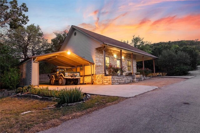 property exterior at dusk with covered porch, driveway, stone siding, and an attached carport