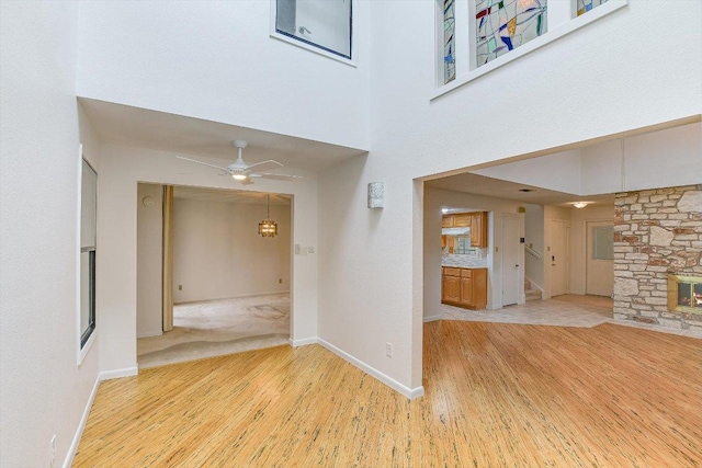 8518 Fathom Cir Unit 107, Austin, TX 78750 - unfurnished living room featuring wood finished floors, a stone fireplace, a ceiling fan, a high ceiling, and baseboards