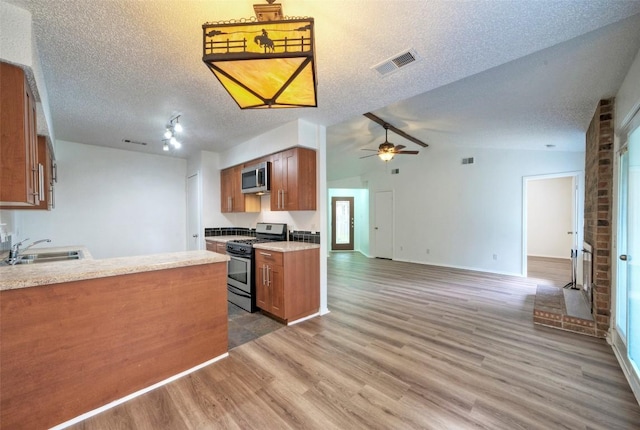 kitchen featuring visible vents, vaulted ceiling, brown cabinets, wood finished floors, and stainless steel appliances