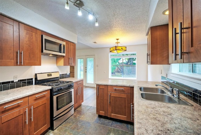 kitchen with brown cabinetry, a peninsula, a textured ceiling, a sink, and stainless steel appliances