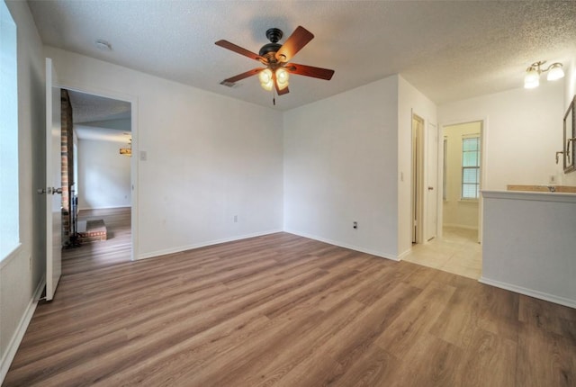 empty room with ceiling fan, a textured ceiling, baseboards, a healthy amount of sunlight, and wood finished floors