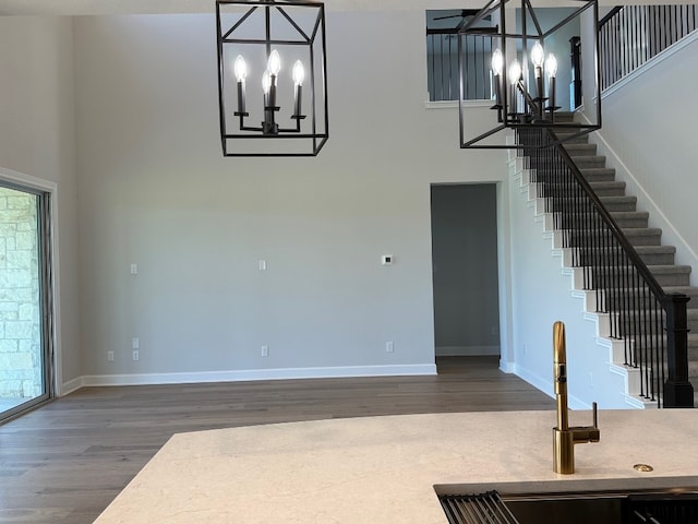 unfurnished living room with wood finished floors, a sink, a high ceiling, and a notable chandelier