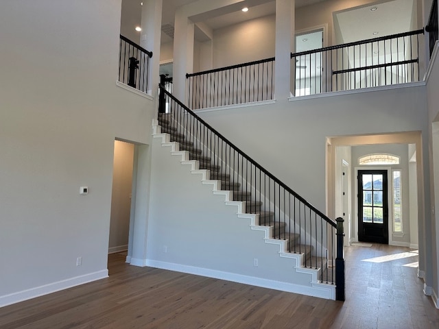 stairway with wood finished floors, baseboards, and a high ceiling