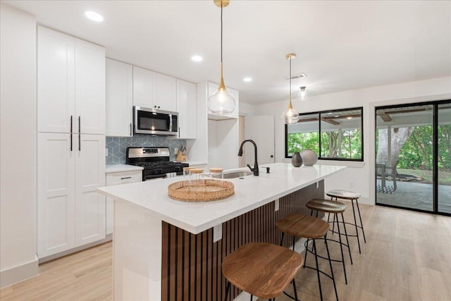 kitchen with a center island with sink, white cabinetry, light wood finished floors, backsplash, and stainless steel appliances