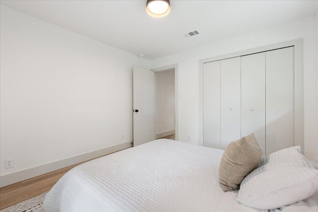 bedroom featuring baseboards, wood finished floors, visible vents, and a closet