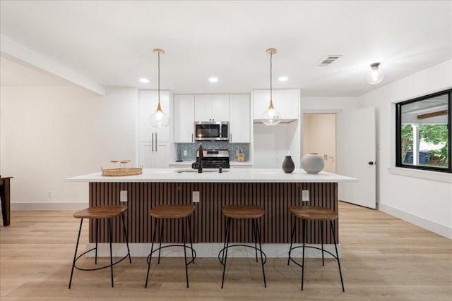 kitchen featuring visible vents, an island with sink, white cabinetry, a sink, and stainless steel appliances