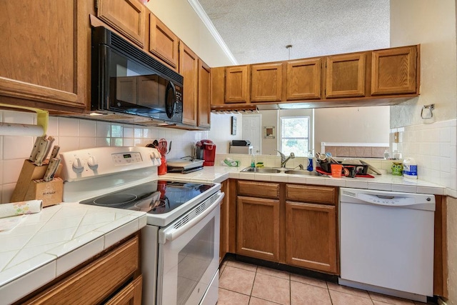 kitchen with white appliances, backsplash, brown cabinetry, and a sink