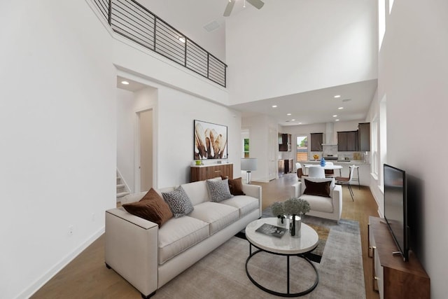 living area featuring light wood-type flooring, a ceiling fan, stairs, and a towering ceiling