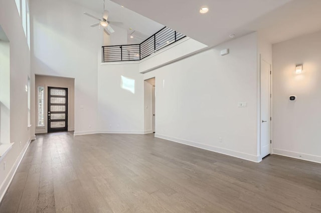 unfurnished living room featuring baseboards, a towering ceiling, ceiling fan, and wood finished floors
