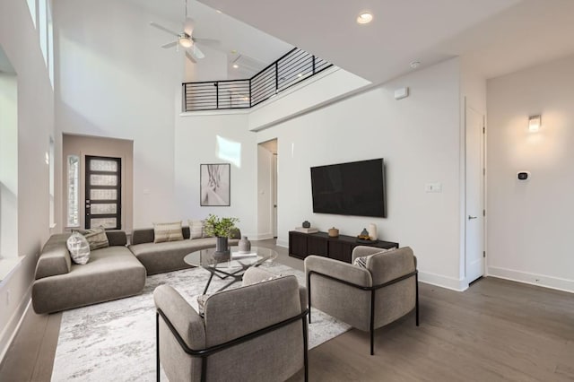living area with a high ceiling, a ceiling fan, baseboards, recessed lighting, and wood finished floors