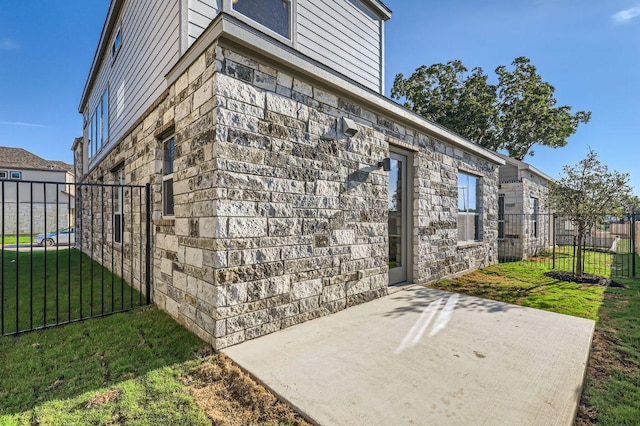 view of side of home with a patio area, fence, a yard, and stone siding