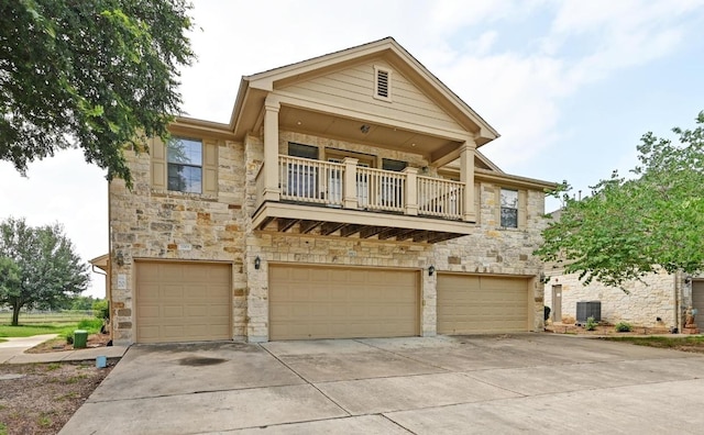 view of front of property with central AC, stone siding, a garage, a balcony, and driveway