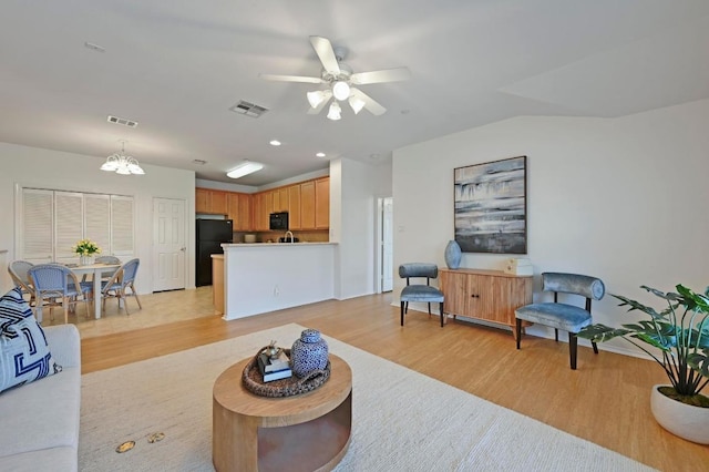 living room with visible vents, light wood-style flooring, and ceiling fan with notable chandelier