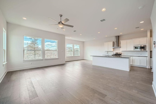 kitchen featuring wall chimney range hood, ceiling fan, stainless steel appliances, open floor plan, and tasteful backsplash