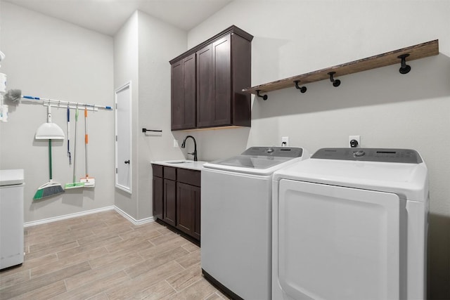 washroom featuring cabinet space, washer and dryer, a sink, light wood-style floors, and baseboards