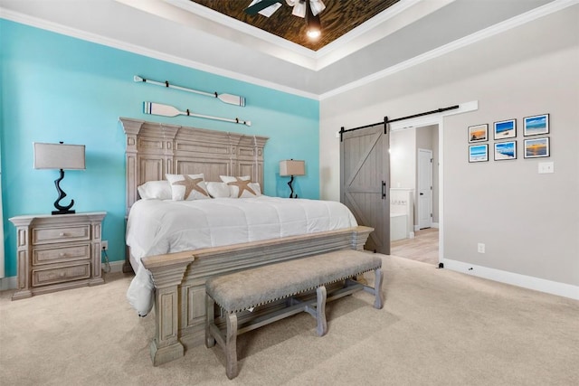 carpeted bedroom with ensuite bathroom, a barn door, baseboards, ornamental molding, and a tray ceiling