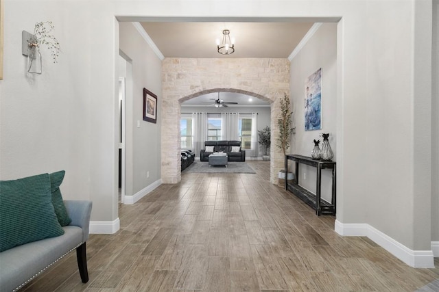 hall featuring crown molding, arched walkways, and light wood finished floors