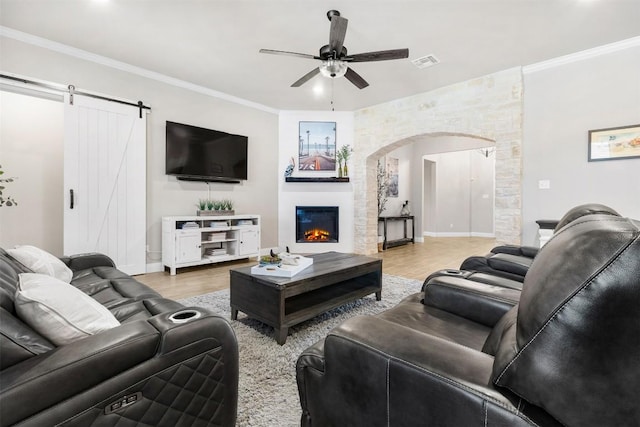 living area featuring arched walkways, a glass covered fireplace, light wood-style flooring, a ceiling fan, and visible vents