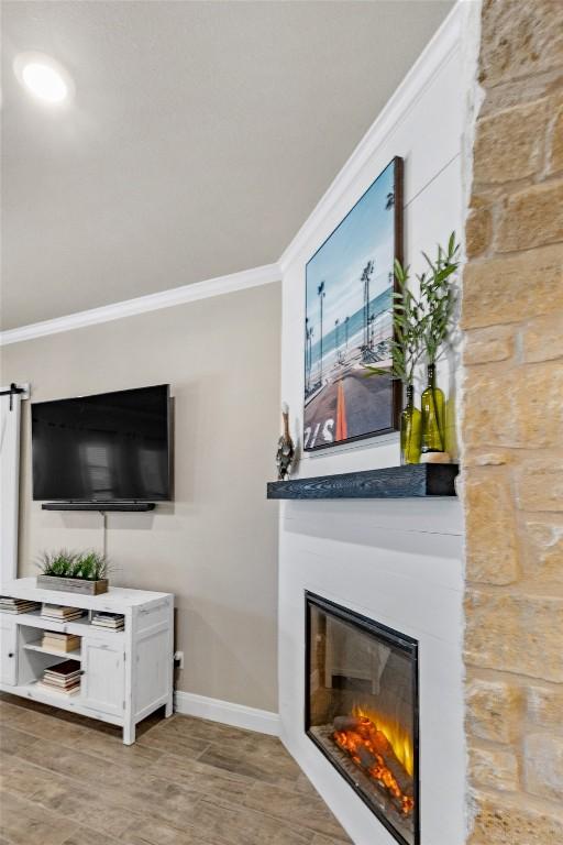 living area featuring baseboards, a glass covered fireplace, ornamental molding, and light wood-type flooring
