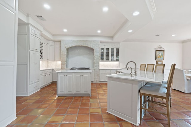kitchen with ornamental molding, a kitchen island with sink, a breakfast bar, a sink, and backsplash