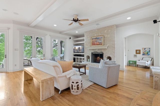 living room featuring a fireplace, beamed ceiling, light wood-type flooring, arched walkways, and a ceiling fan