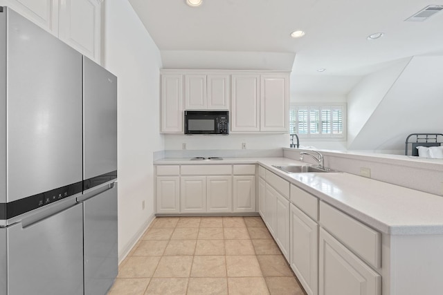 kitchen with black microwave, a sink, freestanding refrigerator, a peninsula, and visible vents